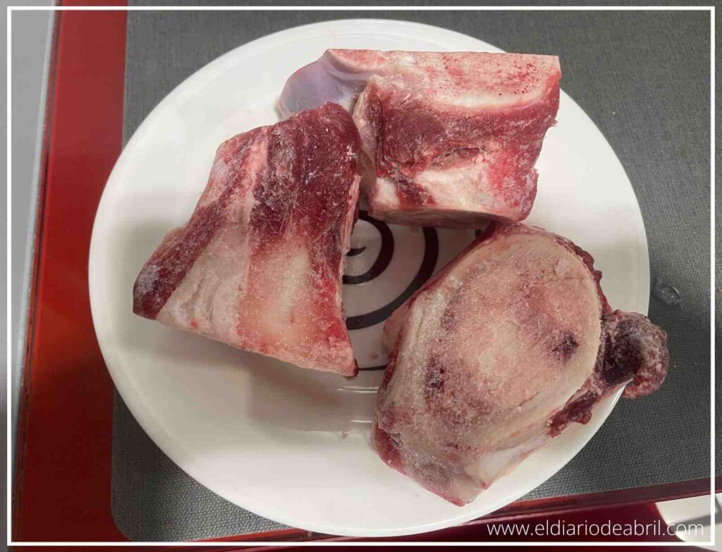Tres trozos de hueso de caña de ternera crudos y frescos colocados sobre un plato blanco